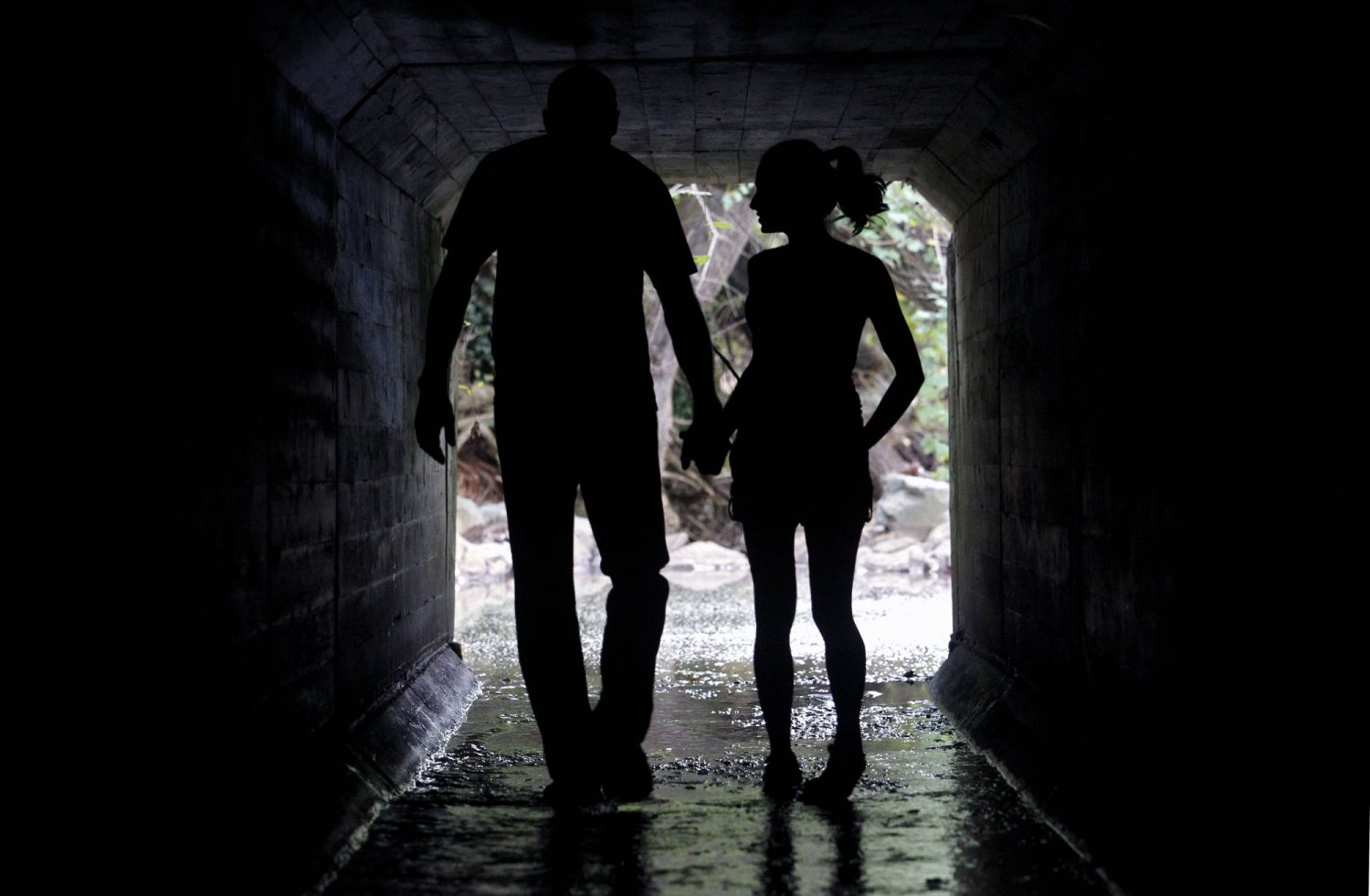 2 people, holding hands, walking in a tunnel waterway